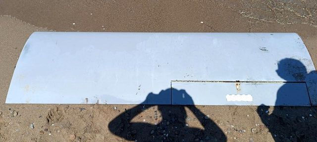 Coast Guard examines a drone wing piece on the beach
