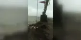 Rüzgarda kopmak üzere olan Türk bayrağını kepçeye çıkarak yerinden aldı