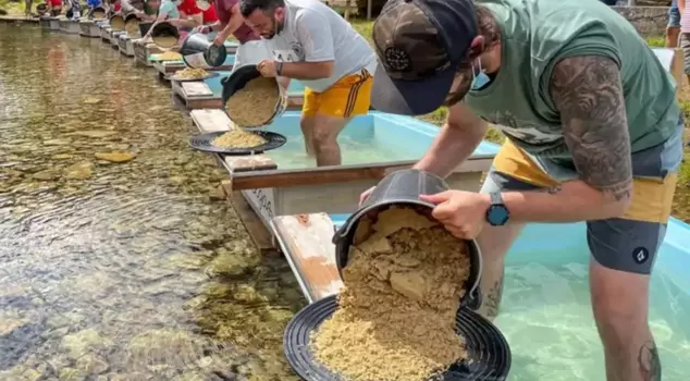 It appears in the riverbed, gathering handfuls with a pan in hand.