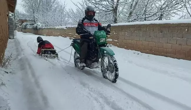 Motosiklete bağladığı kızaklarla çocukları karda eğlendirdi