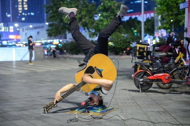 Kafası üstünde durarak hem gitar çalıyor hem de şarkı söylüyor