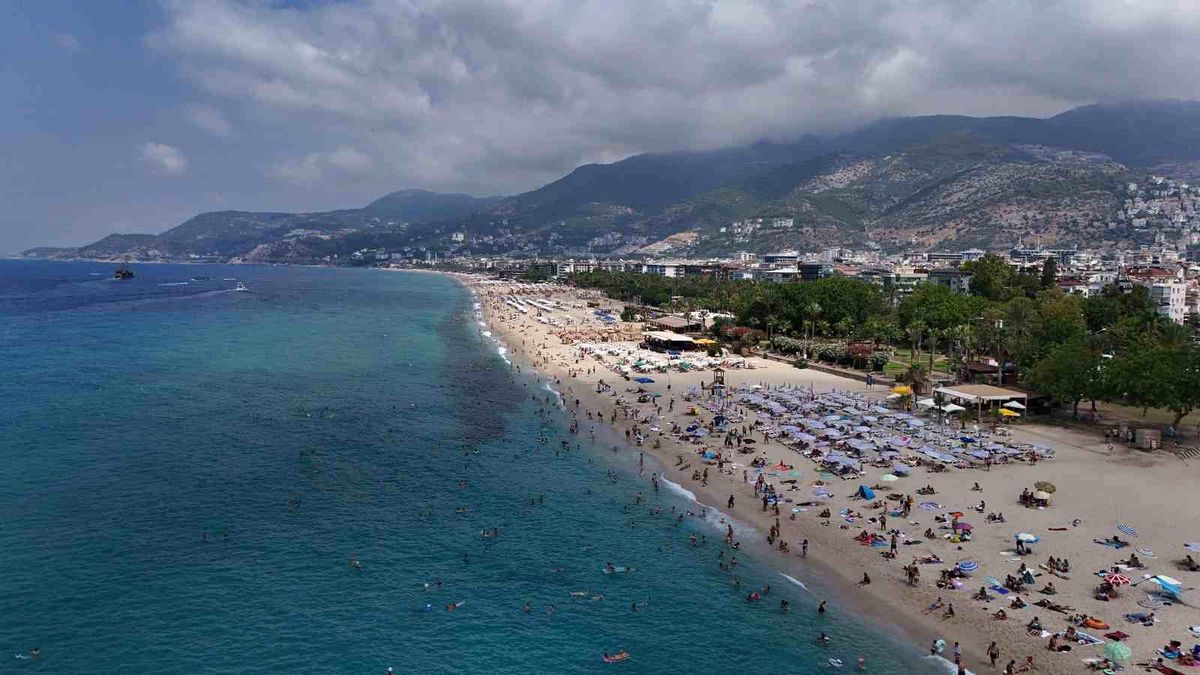 Alanya'da güneşli bir günde Kleopatra Plajı'nda denize giren ve güneşlenen turistler.