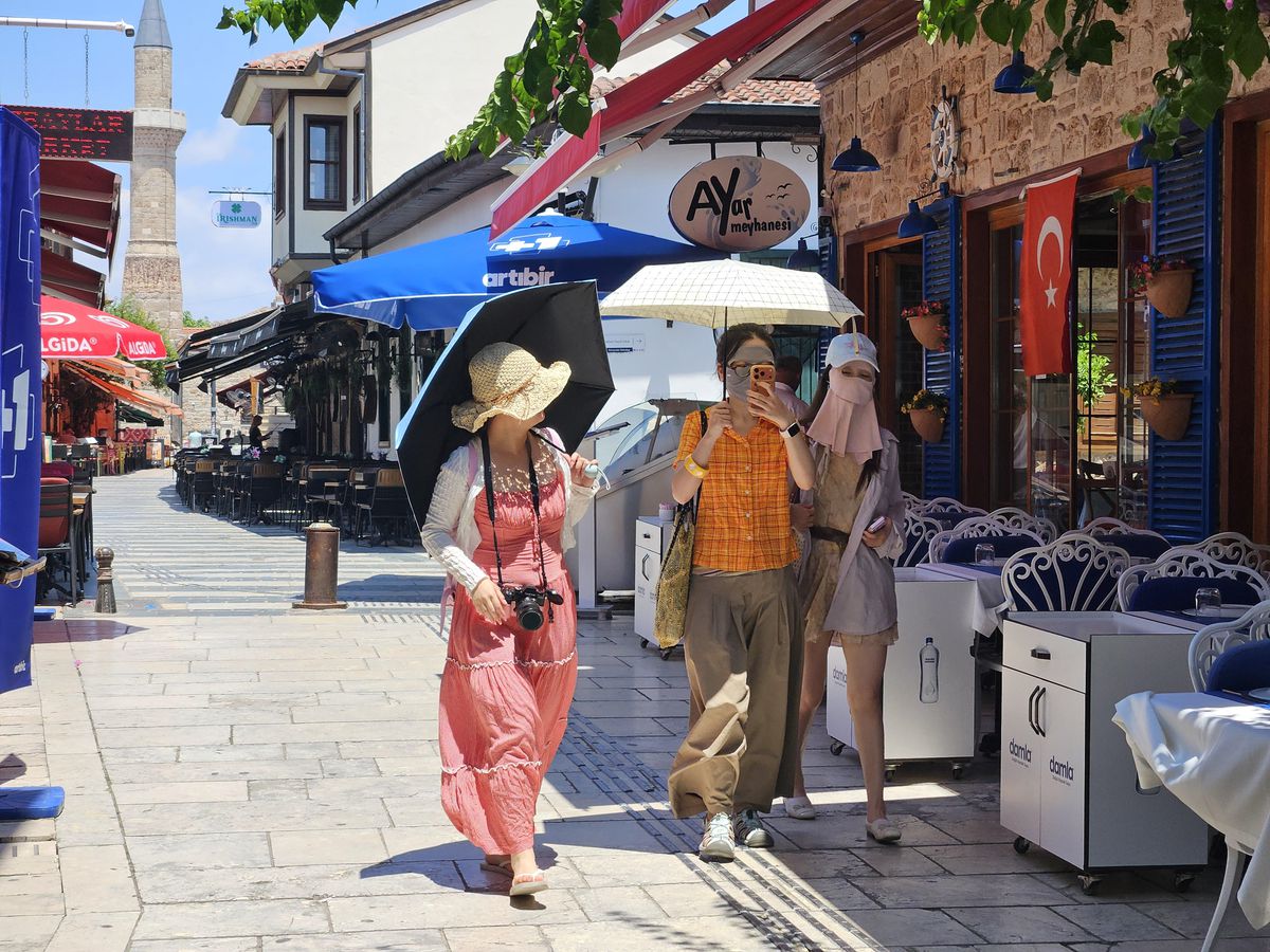 Antalya'da sıcaktan korunmak için yüzünü maske ve şemsiye ile kapatan Uzak Doğulu turistler.