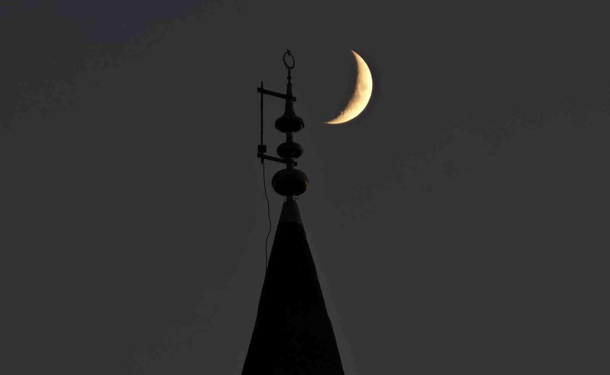 Ahlat'ta akşam gökyüzündeki hilalin, bir cami minaresindeki hilal ve yıldız alemiyle aynı karede göründüğü manzara.